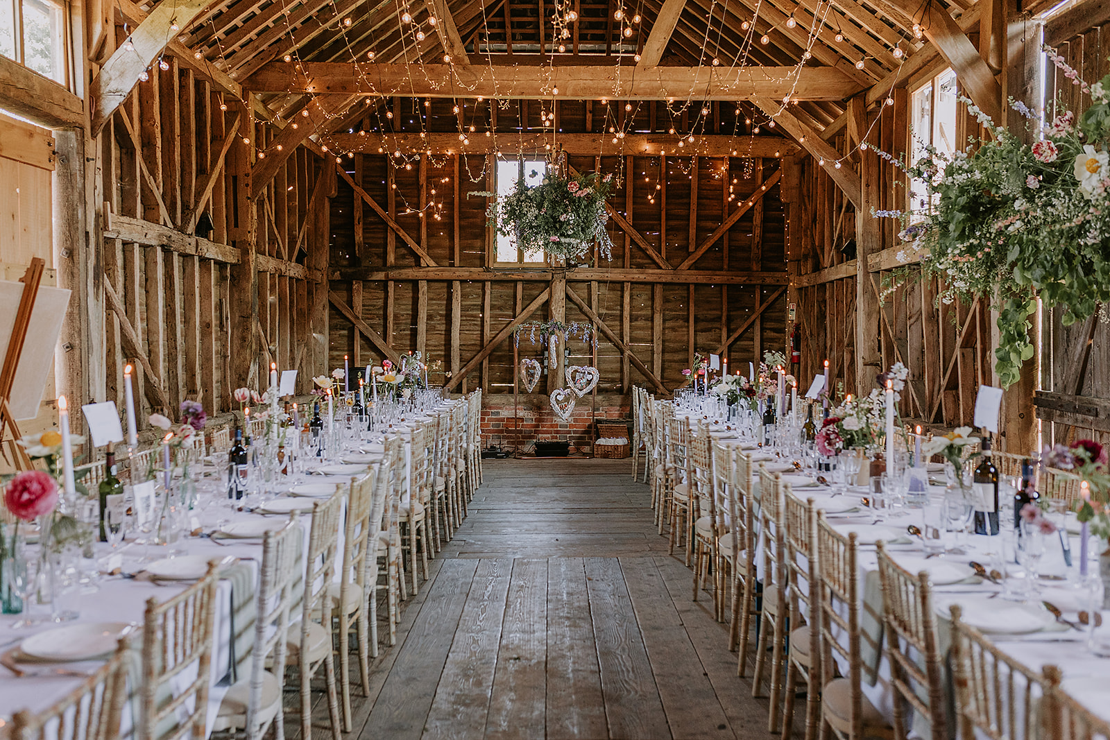 Authentic timber barn wedding reception at The Secret Barn with white linens and seasonal flowers.